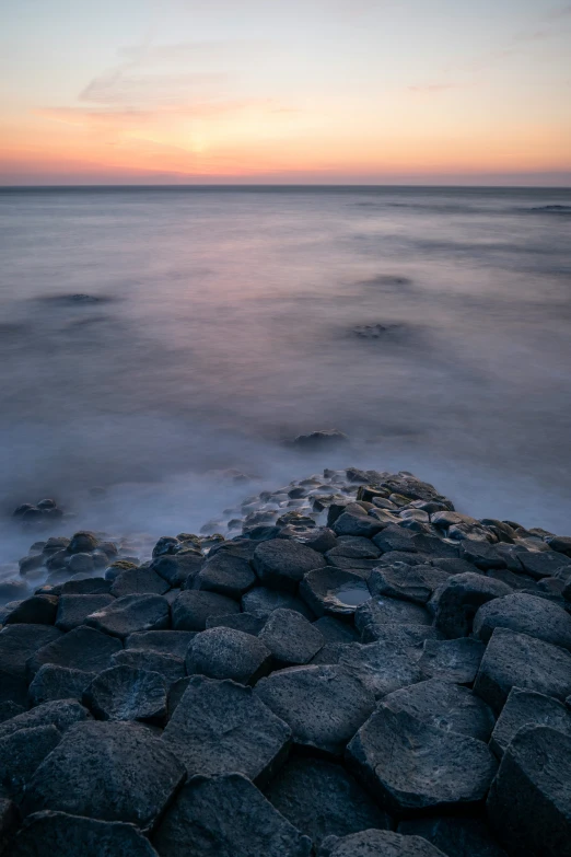 a rocky shoreline is pographed against a cloudy sunset