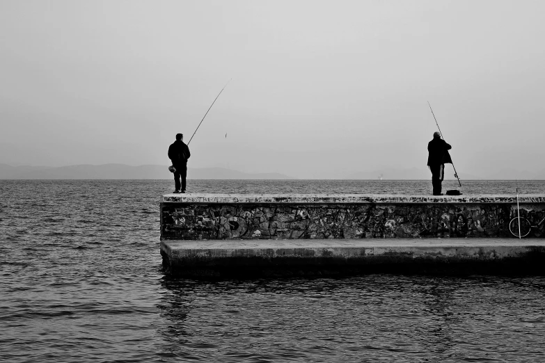 two men are standing on a pier fishing