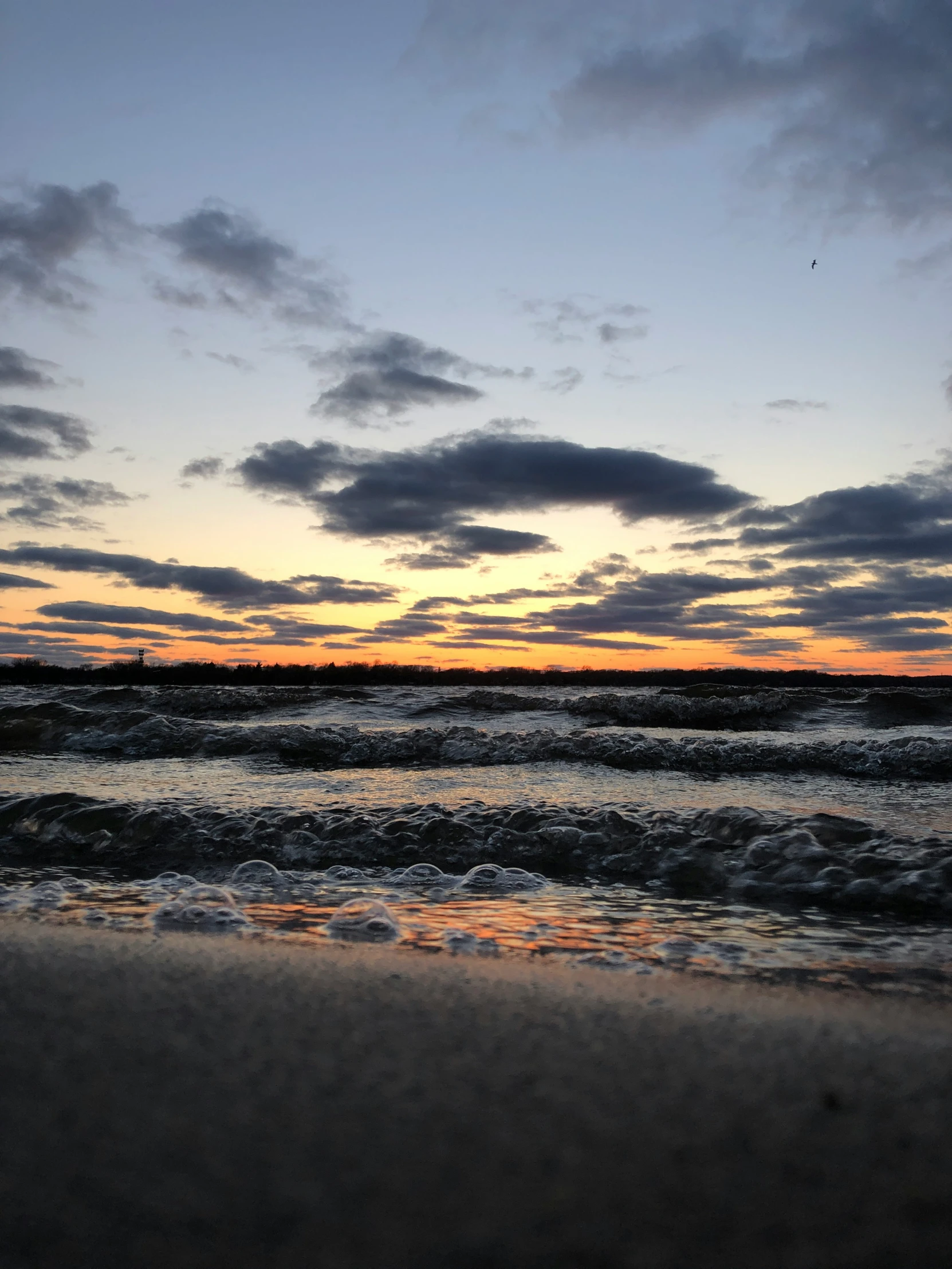 the sky over the water and beach has waves rolling in to shore