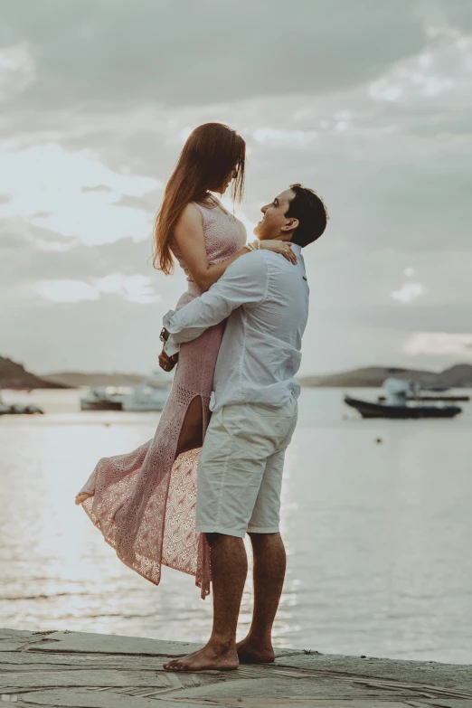 a young couple is standing together by the water looking at each other