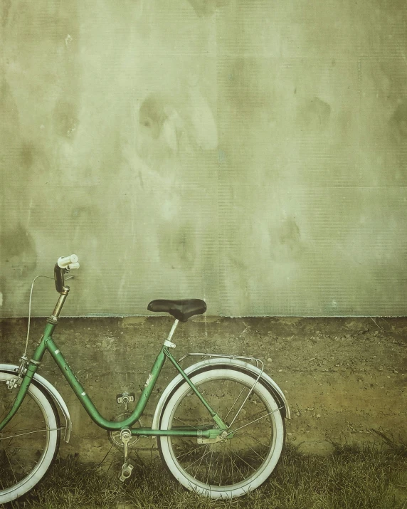 an old vintage green bicycle leans against a stone wall