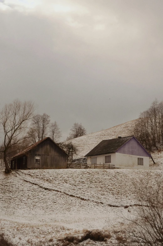 an empty snowy field with some barns and buildings in the snow