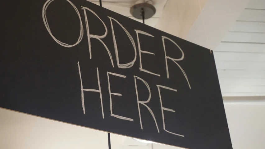 a black sign with an order here written underneath