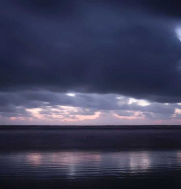 clouds over water with a lone sailboat on the horizon