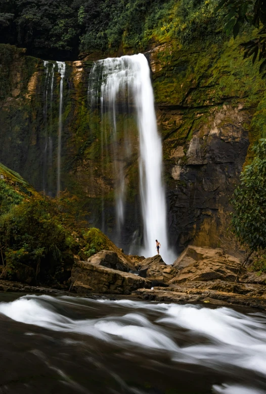 a person standing at the base of a large waterfall