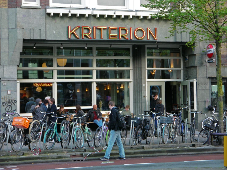 people stand outside of a restaurant with lots of bikes