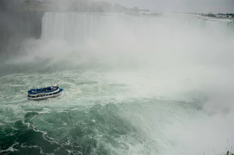 a boat in the middle of a river next to a large waterfall