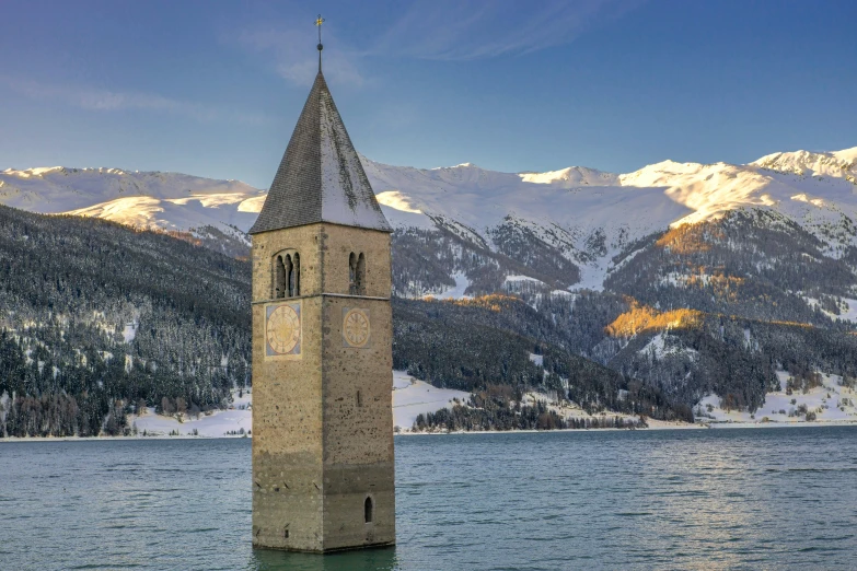 a tall tower towering over a lake surrounded by mountains