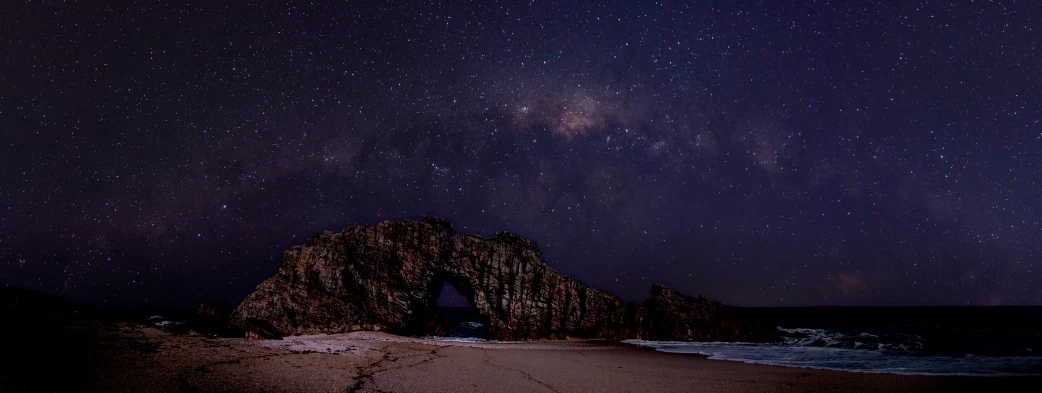 the night sky shows stars and a large rock at the beach