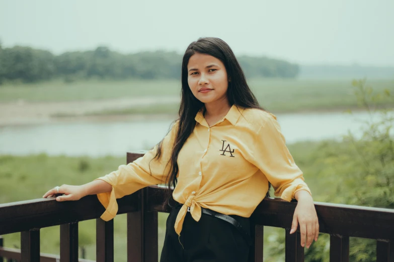 a beautiful young woman sitting on a rail near a river