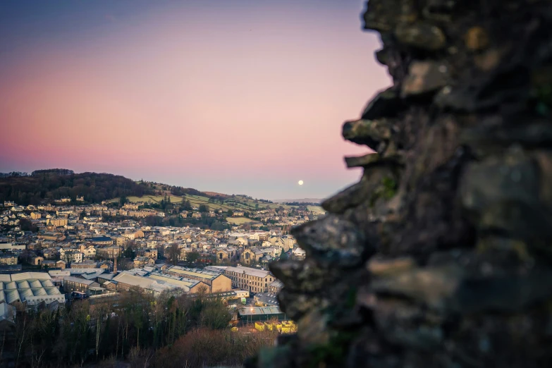 a view from a stone wall looking at a city and a distant moon