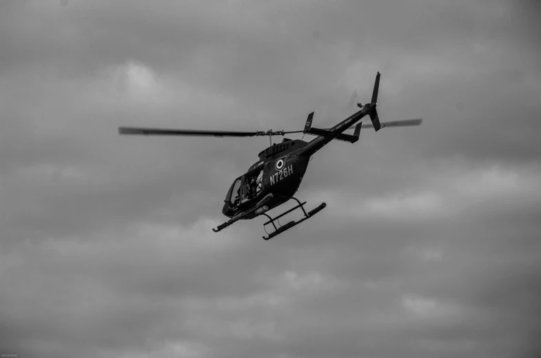 black and white image of a helicopter flying in cloudy sky