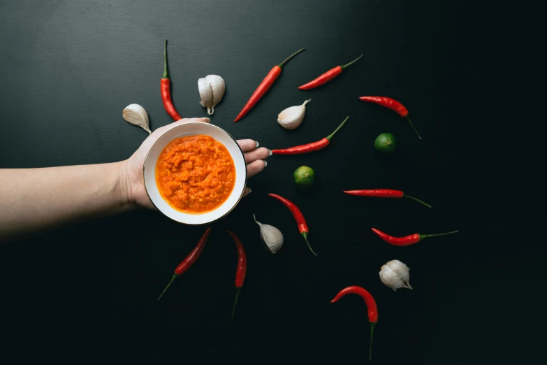 several peppers and white garlic and one being held over a small bowl of food