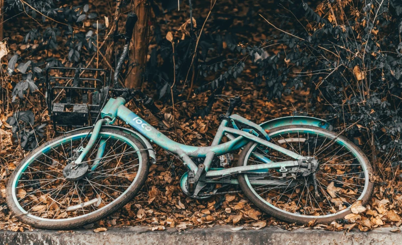 a blue bicycle sitting in a pile of leaves