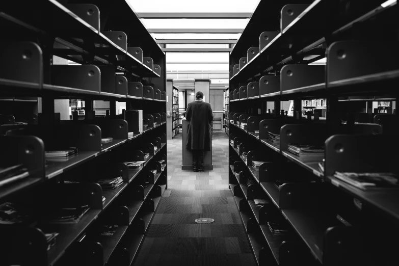 a man with luggage stands in an aisle of many large shelves