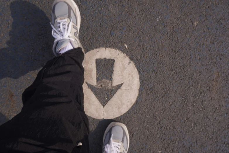 the person's white shoes are standing on the street with an arrow painted on the pavement