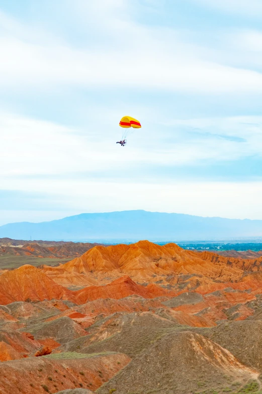 a yellow parachute is flying over rocky terrain