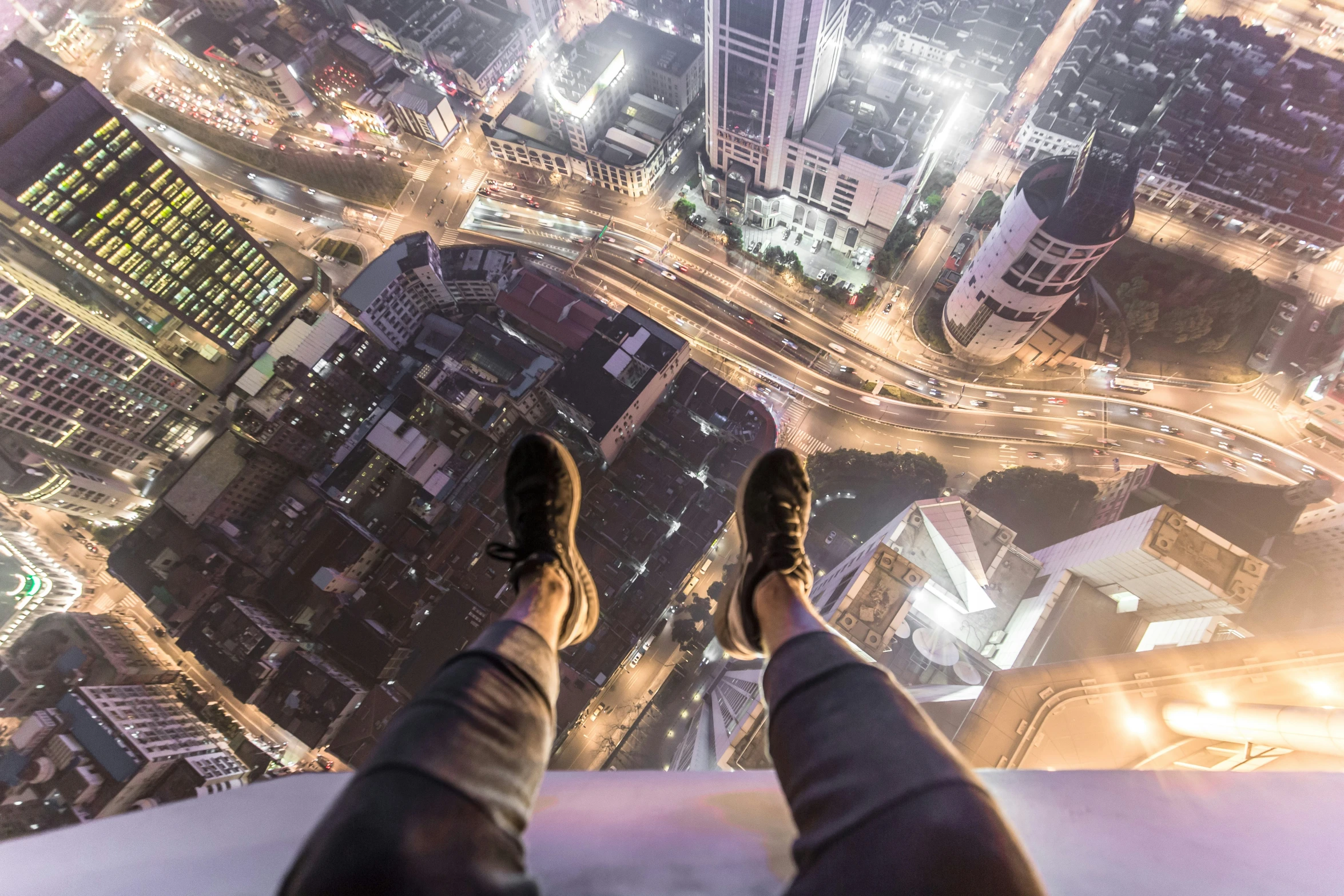 man standing on ledge of high rise building looking at city from top