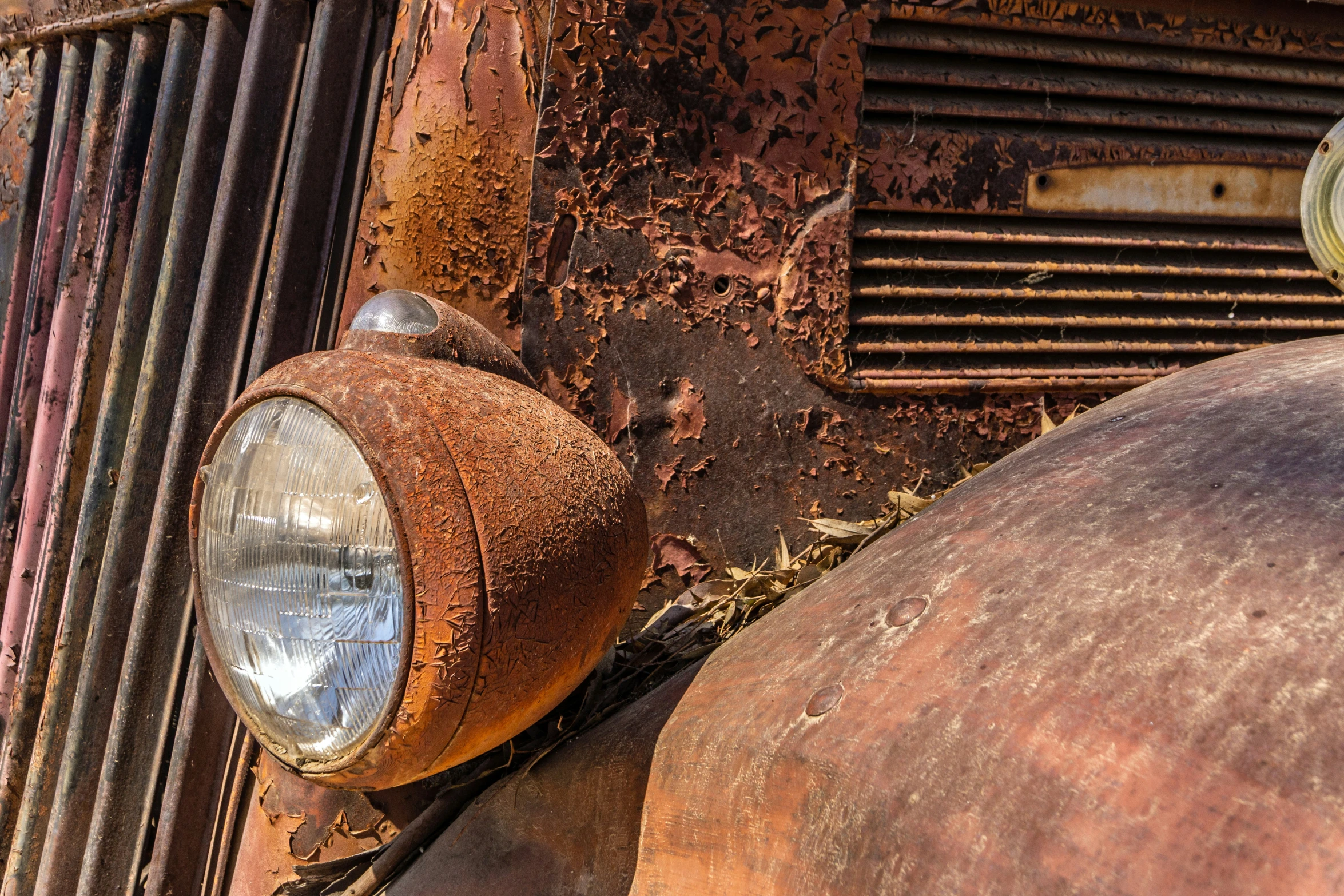 rusted out car headlights and hood ornaments are shown on the front of this old rusty car