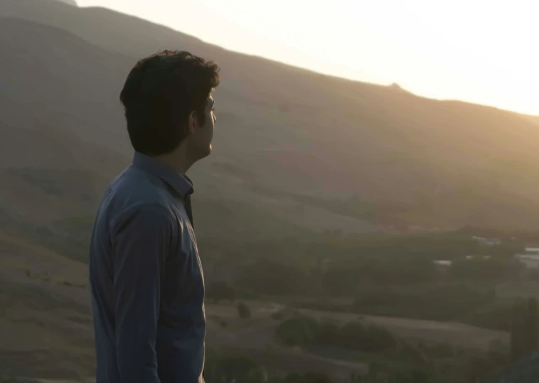 a man standing in front of the sun on top of a hill