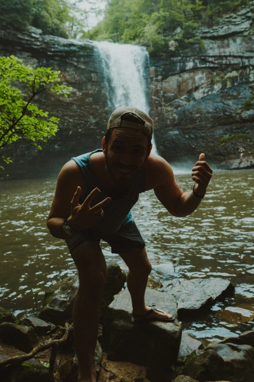 a man standing next to a waterfall and rock pool