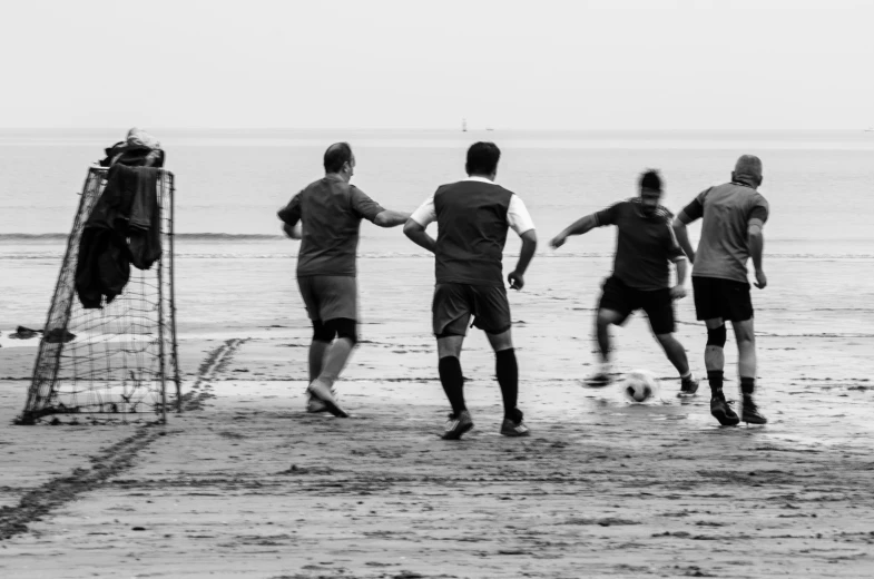 a group of people standing around a soccer goal on top of a beach
