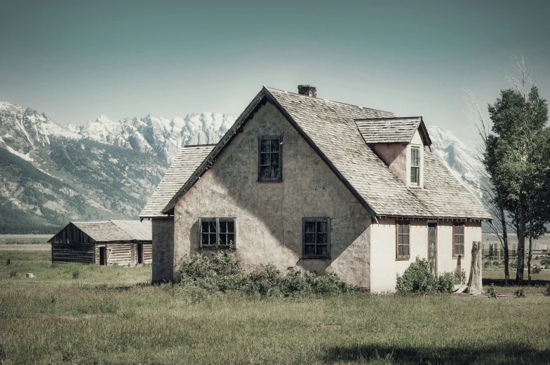 an old house sitting on a mountain with a field next to it