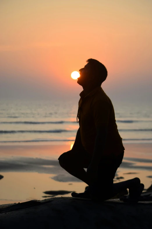 a man kneeling in front of the sun on the beach