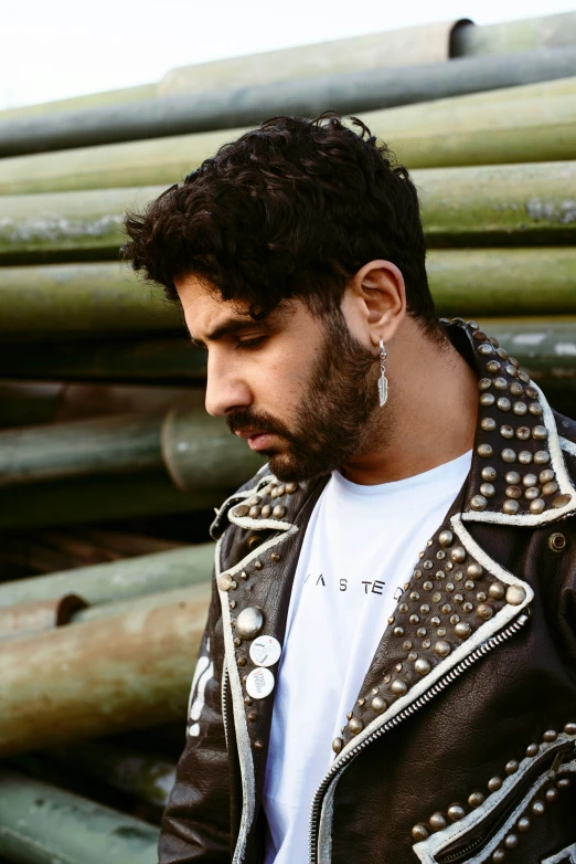 man in leather jacket standing next to stacks of pipe