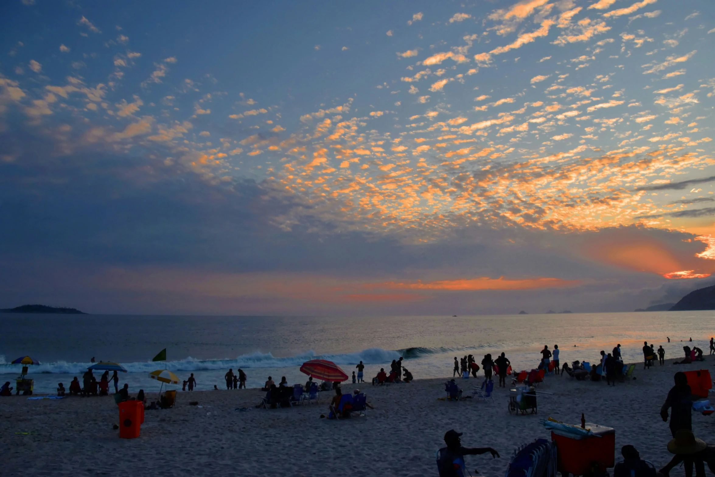 many people are standing on the beach at sunset