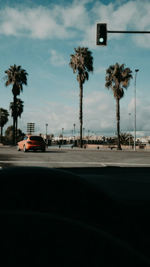 a red car drives down the street past palm trees