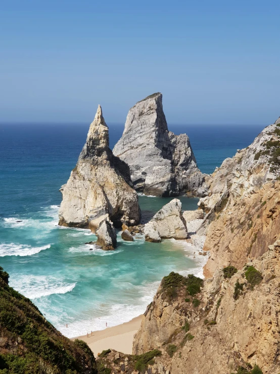 two very tall rocks by the ocean near some water