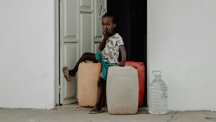 a young black boy sitting in an open door with a bag and two bags