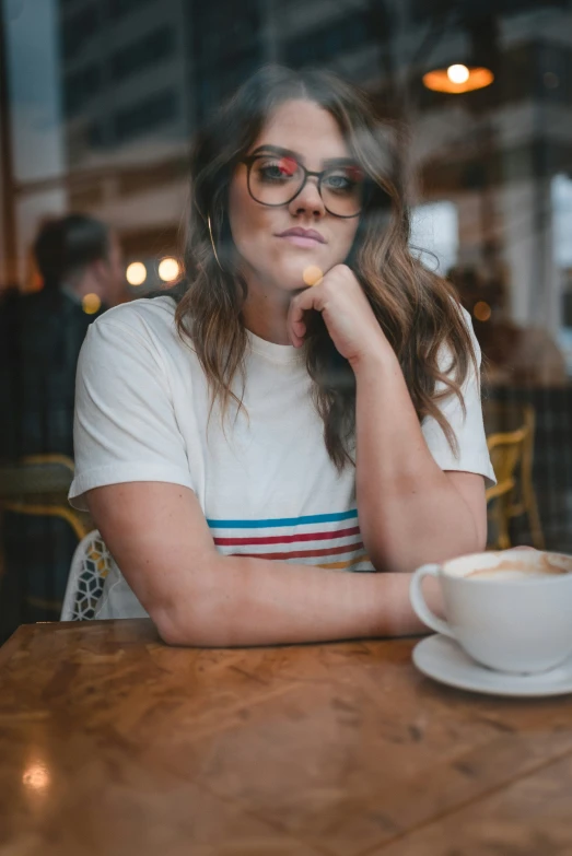 a woman wearing glasses while sitting in front of a coffee