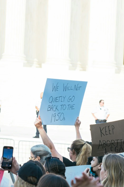 people hold signs as they gather for a rally