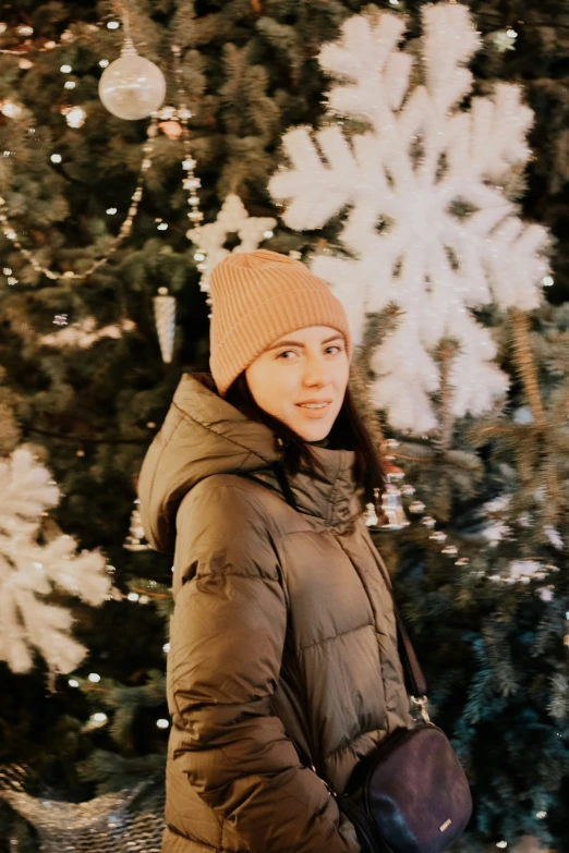 young woman standing in front of christmas tree wearing warm clothing
