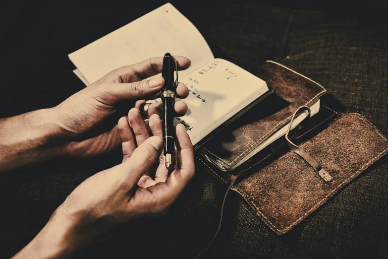 a person sits at a table with an opened notebook, pen and pocketbook in his hand