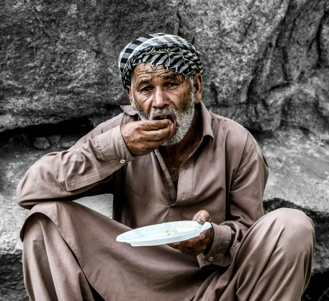 a man sitting in front of some large rocks eating soing