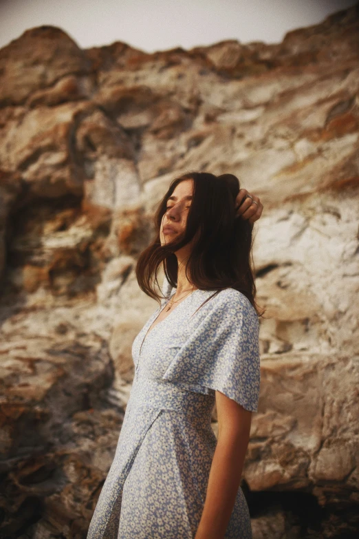 woman in a dress standing near rocky cliffs