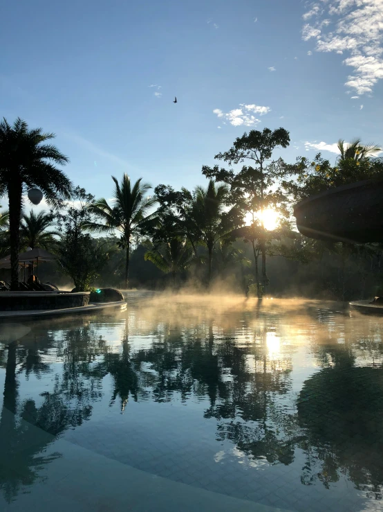 steam rises from the pool at dusk with the sun behind