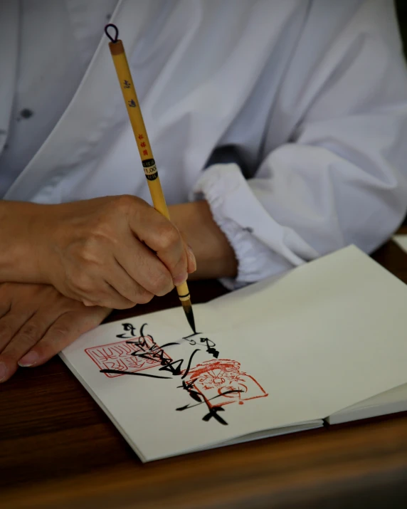 person in white shirt using pencil on a notebook and drawing a figure on the paper