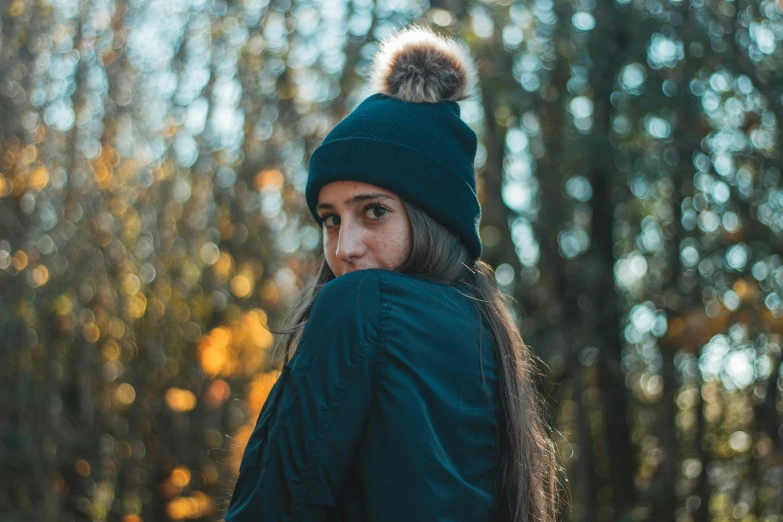 the girl in a green coat is standing near some trees