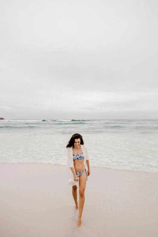 a girl in a bikini walks along the beach