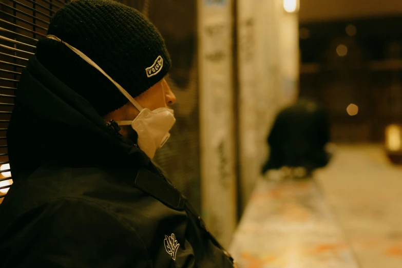 the man wearing a mask and jacket walks on the sidewalk