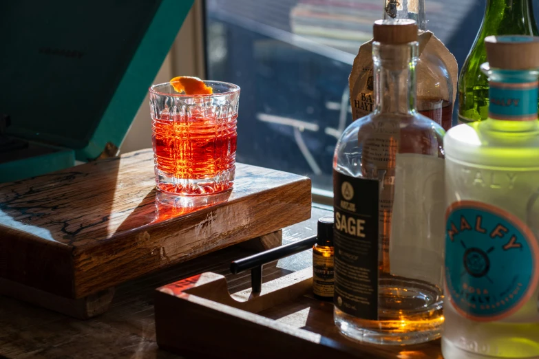 an alcohol glass is on a wood tray near several bottles