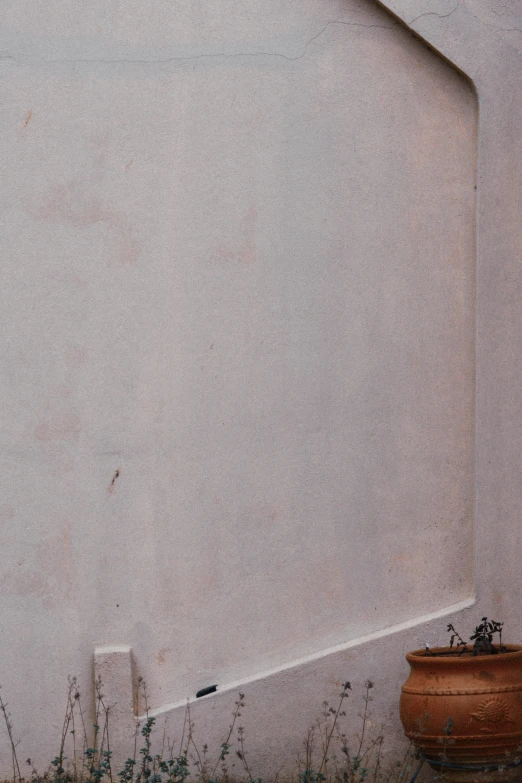 a flower pot next to a wall on the grass