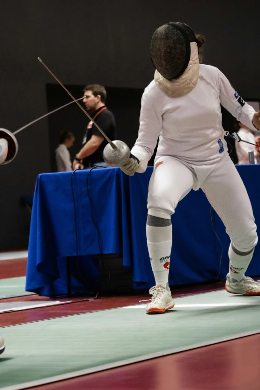 two people wearing white fencing uniforms while standing on the floor