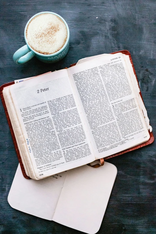 an open book sitting on top of a desk next to a cup of coffee