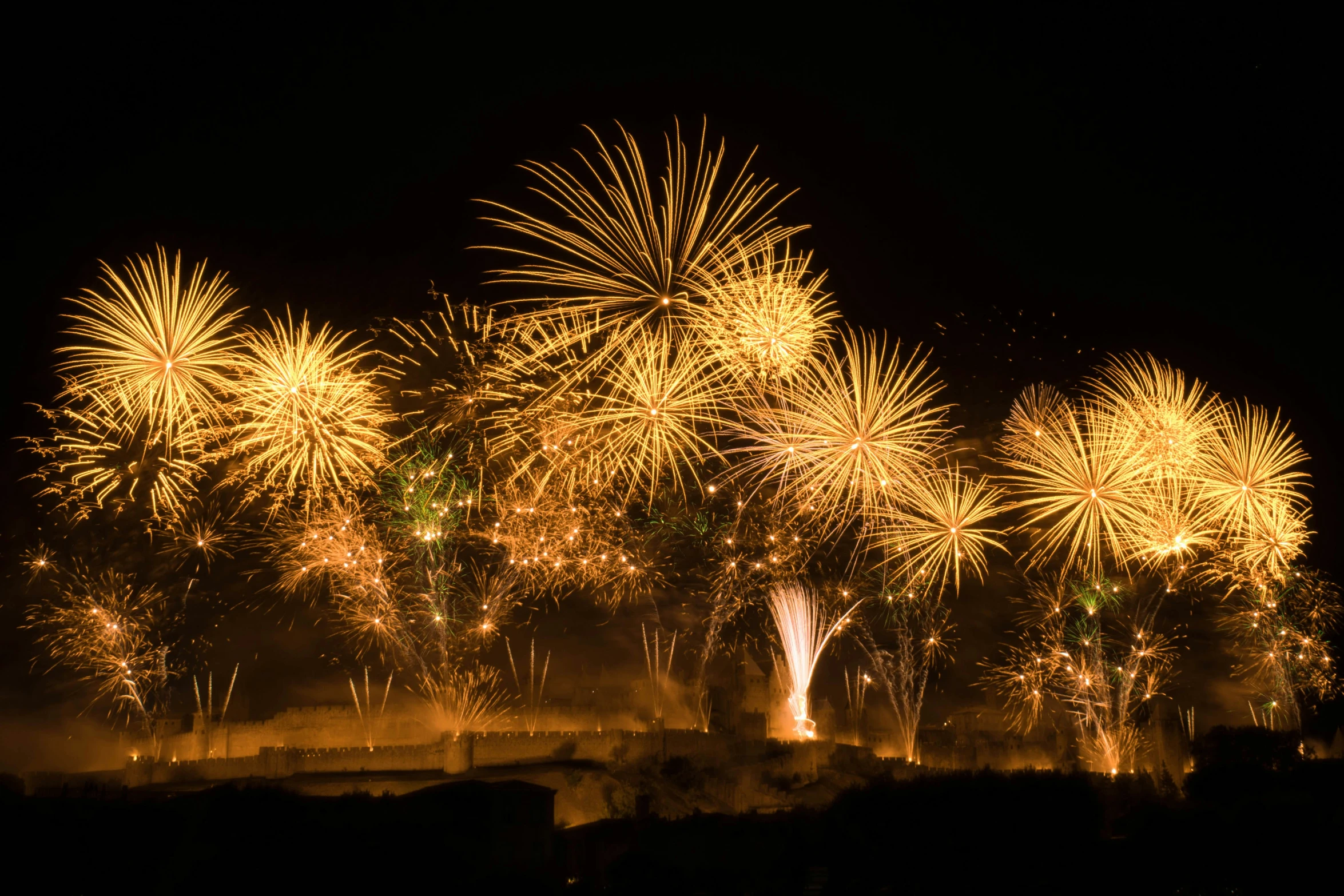 brightly lit fireworks on a black background as seen from an overcast city skyline