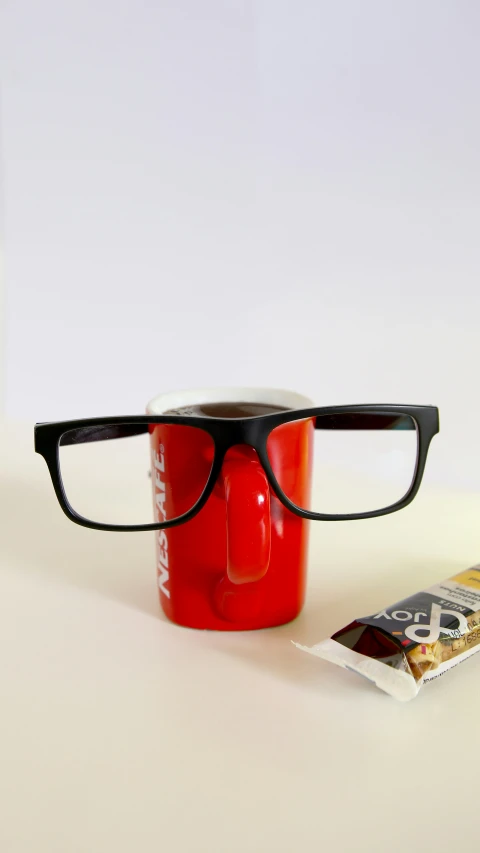 the red coffee cup with glasses is next to the reading glasses